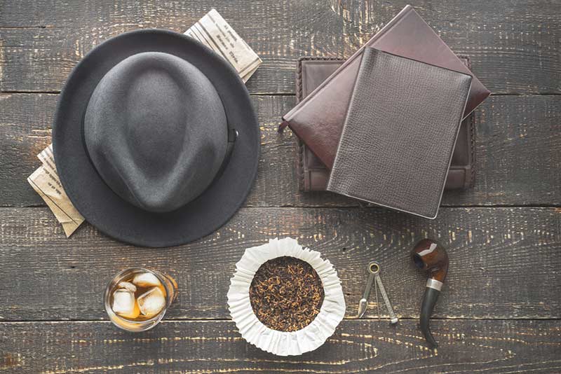 aerial shot of a hat, a drink, some books and a smoking pipe